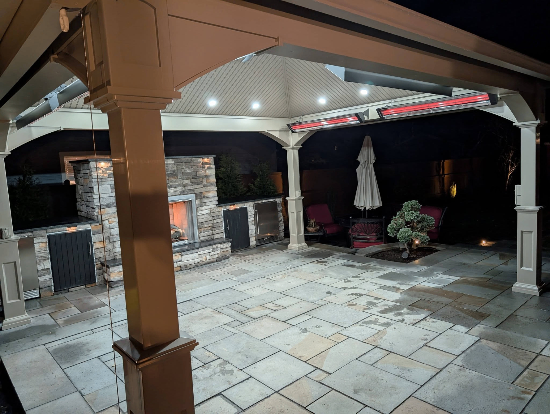 Covered patio with mounted heaters, seating area, and stone fireplace