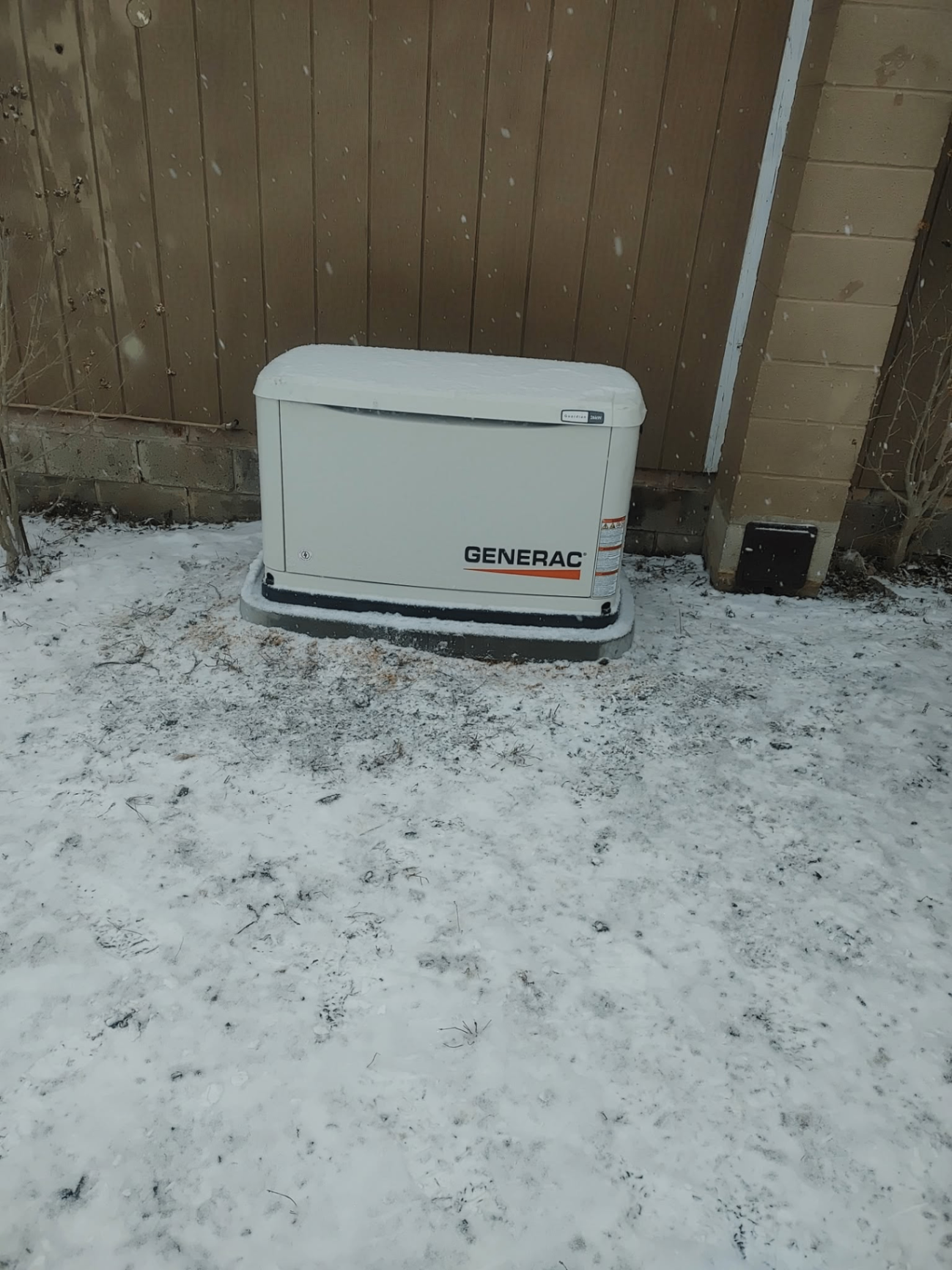 Generac whole-home standby generator installed beside a house during a light snowfall