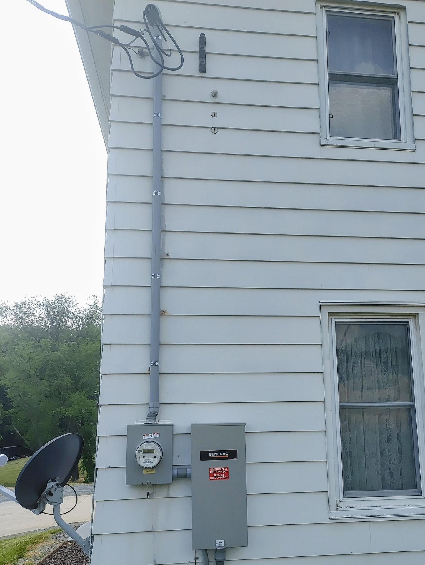 Exterior home wall with meter base, Generac emergency disconnect, and vertical conduit run