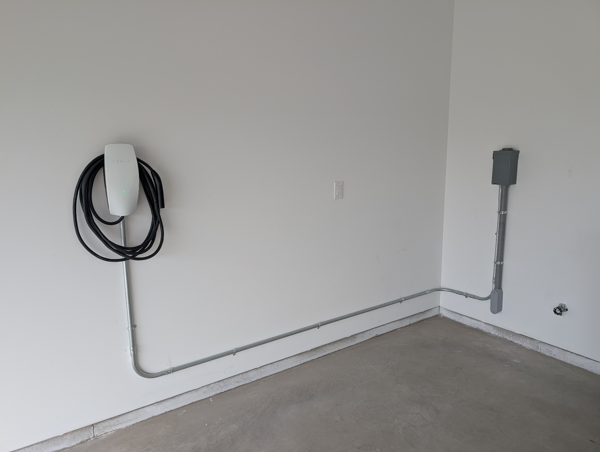 Tesla wall connector EV charger installed in a residential garage with conduit run to a subpanel