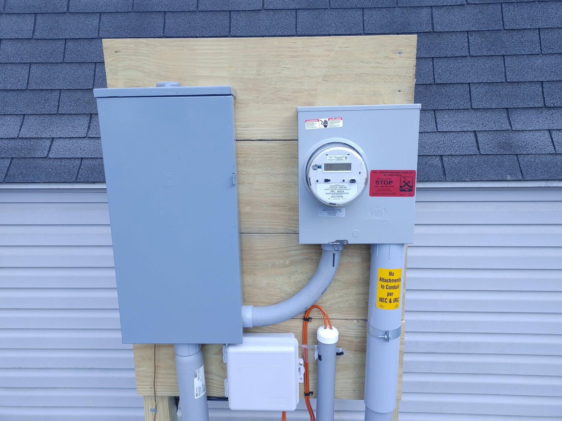 Exterior electrical service equipment with meter socket, conduit, and gray service disconnect mounted on siding