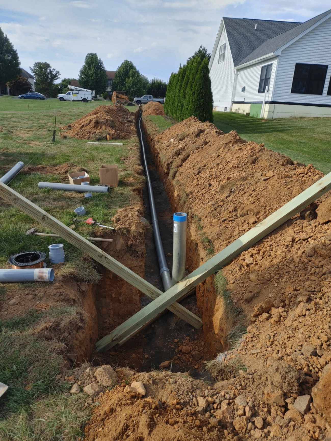 Residential trench with underground conduit run extending across a yard toward a home