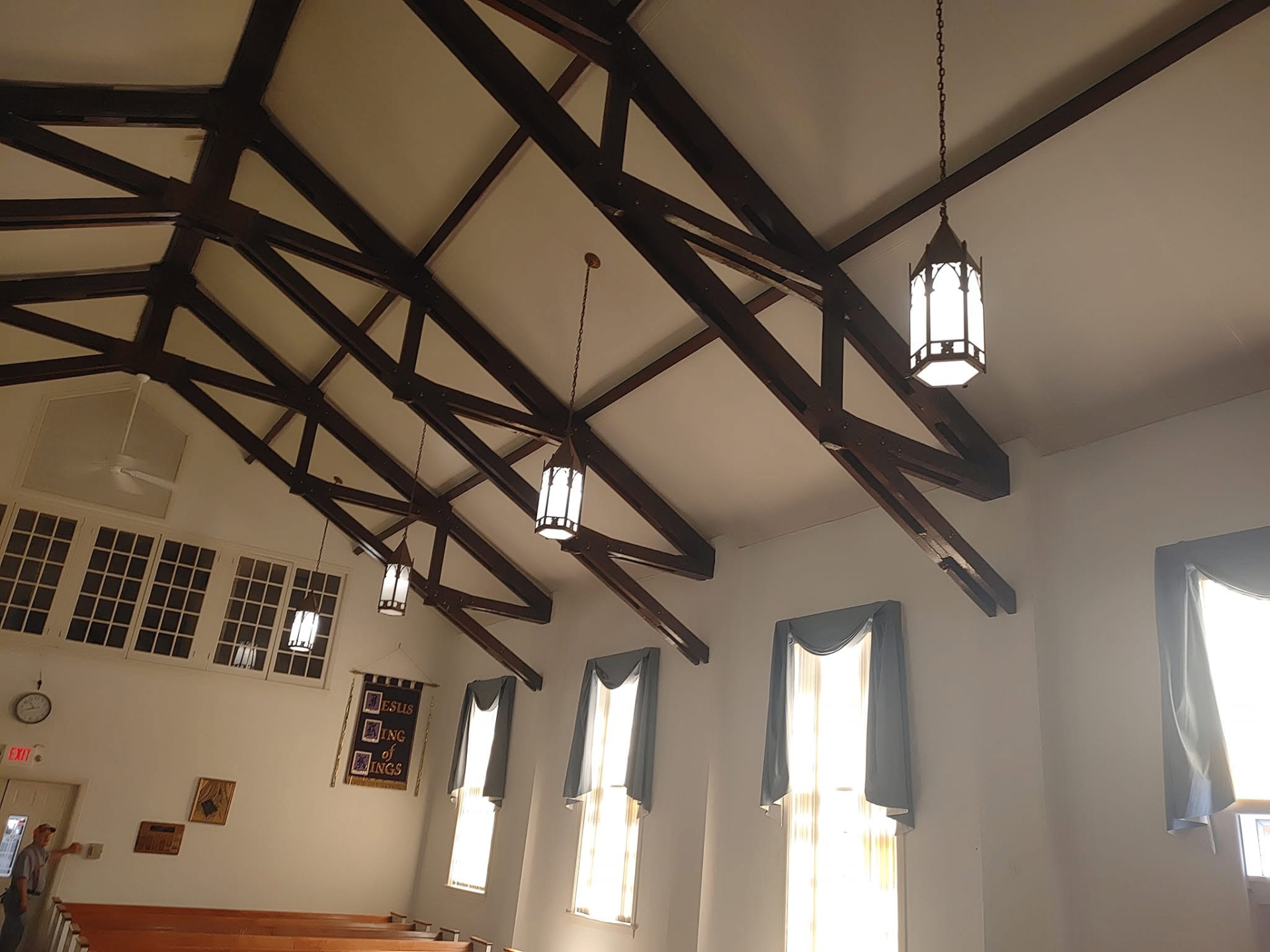 Angled view of church ceiling trusses with hanging light fixtures illuminated
