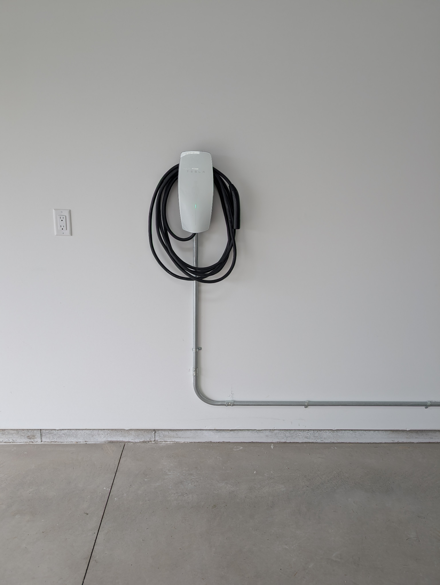 Close-up of a Tesla wall connector mounted in a garage with conduit running down to the floor